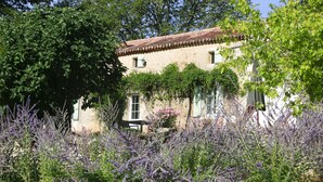 A rustic building with a tiled roof, surrounded by lush greenery and flowering plants.