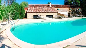 A swimming pool with lounge chairs and a house in the background.