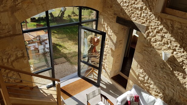 A room with a large glass window, a wooden staircase, a white sofa, and a stone wall.