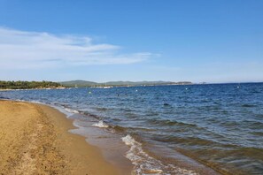 A beach with clear water, a sandy shore, and distant hills.