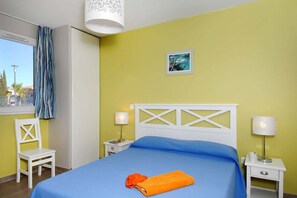 Una habitació d'hotel amb un llit, una cadira, una tauleta de nit, una làmpada i una finestra amb cortines.