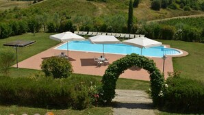 A swimming pool with umbrellas, surrounded by a garden and a wooden deck.