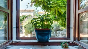 A window with a blue pot of green plants on the sill and a small ceramic pot with a floral design.