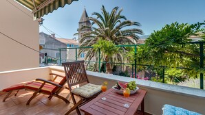 A balcony with a wooden table, two chairs, a bowl of fruit, and two glasses of orange juice.
