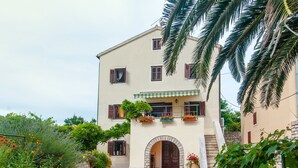 A two-story building with a stone facade, a balcony with potted plants, and an arched entrance.