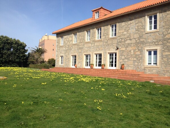 A stone building with a red-tiled roof, multiple windows, and a well-maintained lawn with yellow flowers. - Rural Tourism House, COURTYARD HOUSE (Praia de Lavadores, Vila Nova de Gaia,)