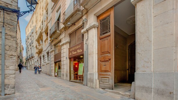 Una calle adoquinada con edificios históricos, un bar restaurante y una puerta de madera.