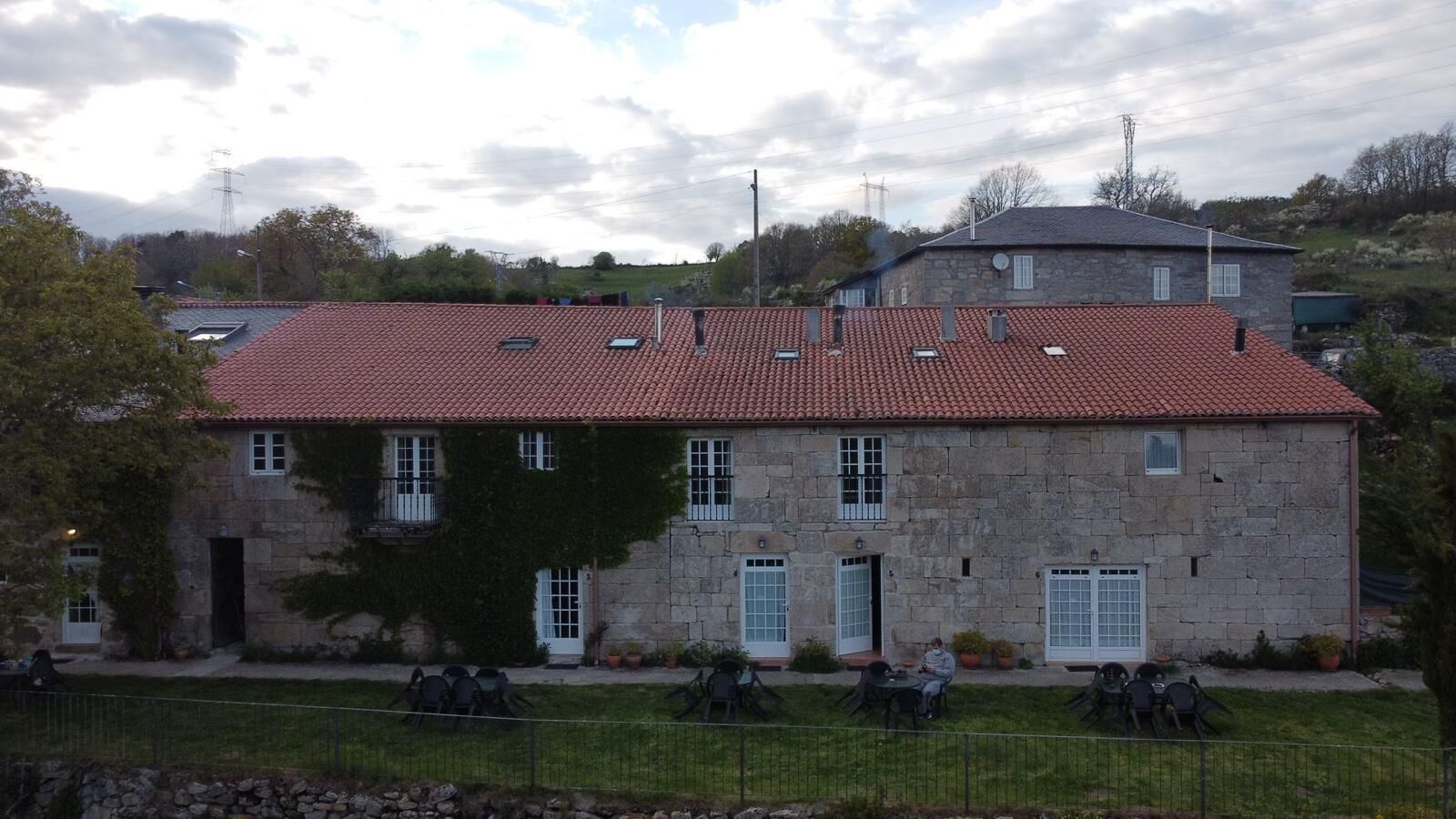 Un bâtiment en pierre avec un toit recouvert de tuiles rouges, de nombreuses fenêtres et un petit jardin agrémenté de chaises.