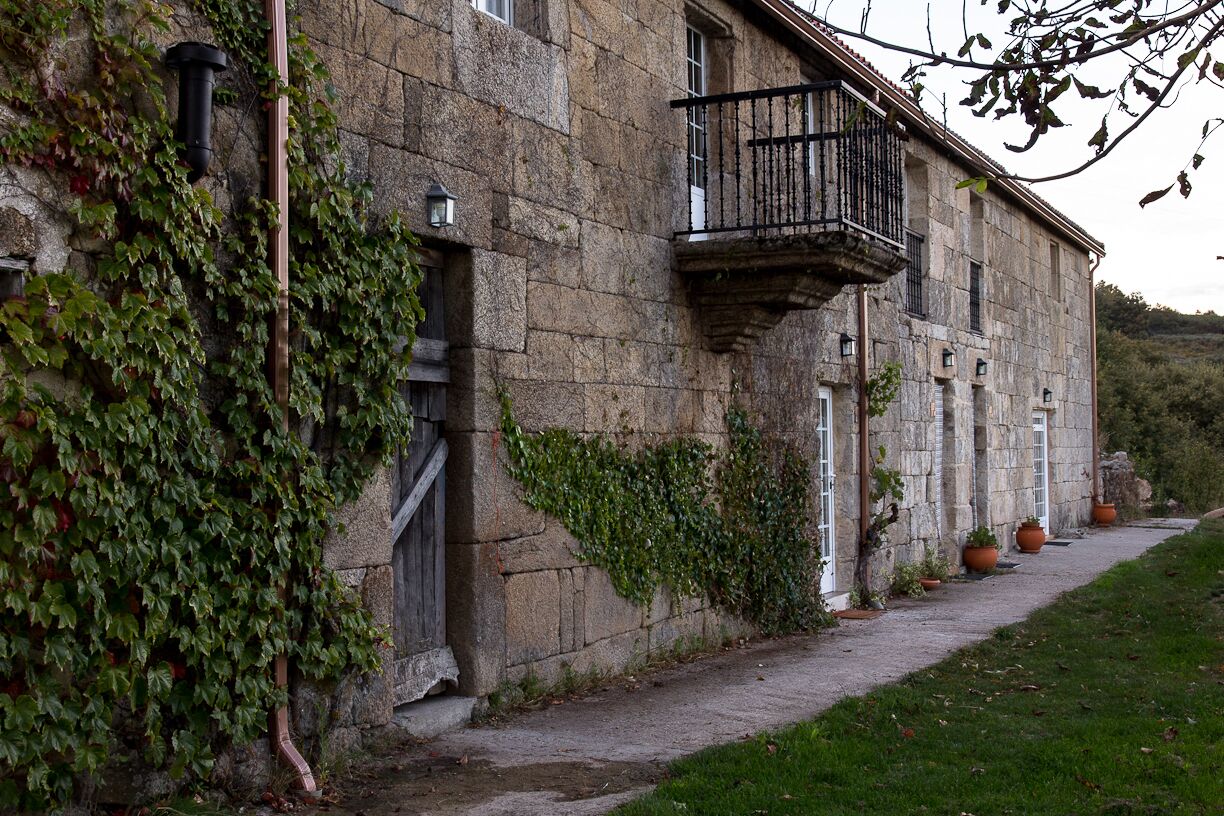 A stone building with a balcony, ivy, and potted plants.
