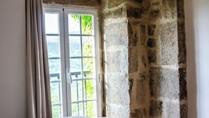 Un muro de piedra, una ventana con vistas a la vegetación y un objeto blanco sobre una superficie.