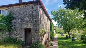 Un edificio de piedra con puerta de madera, un pequeño jardín con sendero y mesas al aire libre.
