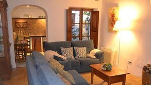 Una sala de estar con un sofá, una mesa de centro y una lámpara. Hay una ventana con cortinas y una puerta que da a otra habitación.