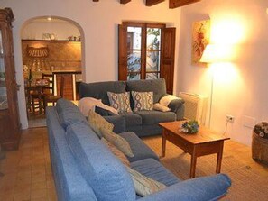 A living room with a sofa, a coffee table, and a lamp. There is a window with curtains and a door leading to another room. - Ca S'angel (Soller)