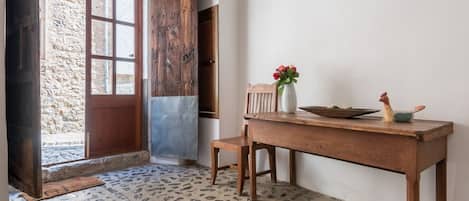 A rustic interior with a wooden door, a stone floor, and a table with a vase of flowers.