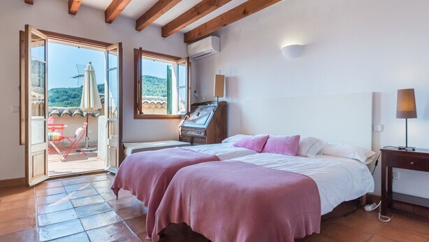 Un dormitorio con dos camas, techo de madera, balcón abierto con sillas y vistas a las colinas.
