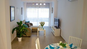 A living room with a sofa, a coffee table, a TV, and a balcony with a view. - Modern apartment in Puerto marina (Benalmádena)