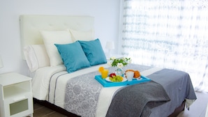 A neatly made bed with a blue and white patterned bedspread, a gray throw blanket, and a tray with breakfast items including croissants, fruit, and a drink. - Modern apartment in Puerto marina (Benalmádena)