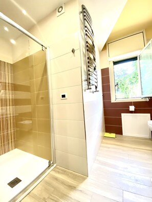 Un baño moderno con cabina de ducha de vidrio, un perchero y una ventana con vistas a zonas verdes.