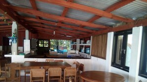 A rustic kitchen with wooden furniture, a dining area with a round table, and a large window. - Eco Hotel El Refugio, In the mountains but near the sea. - ROOM 18 (PLUMA HIDALGO)