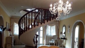 A spacious living area with a large sofa, a glass coffee table, and a grand chandelier. A spiral staircase with dark wood railings leads to an upper level. - VILLA HEMI, WITH DOUBLE ROOMS (Lomitos de Correa)