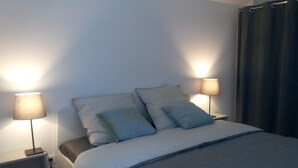 Una cama bien hecha con cubrecama y almohadas grises, flanqueada por mesitas de noche con lámparas.
