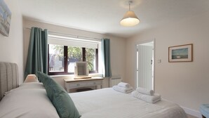 Une chambre à coucher comprenant un lit, un bureau, une chaise, une fenêtre avec des rideaux, un radiateur et une porte.