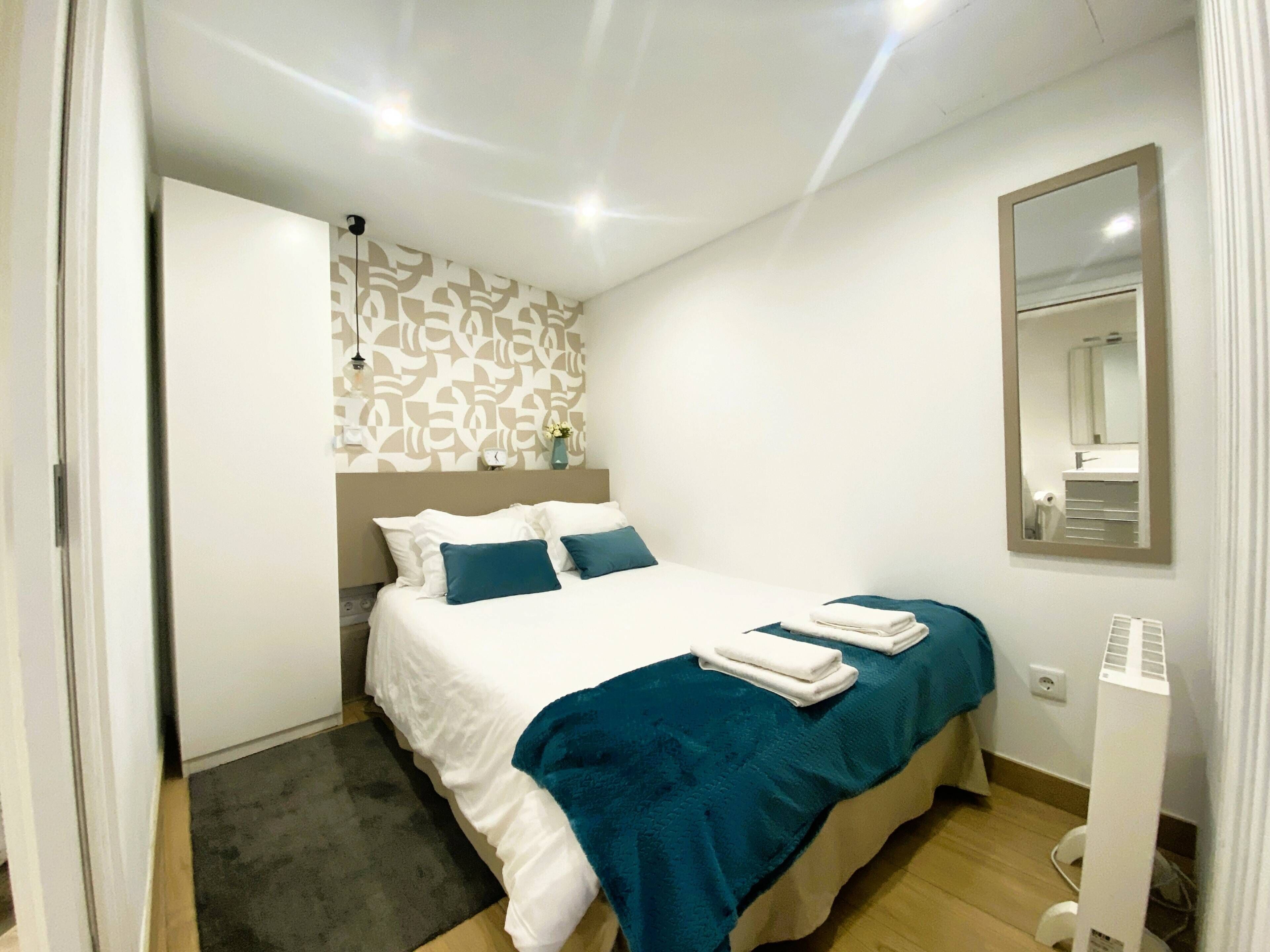 A bedroom with a bed, a bedside table, a mirror, and a wall with a patterned design.