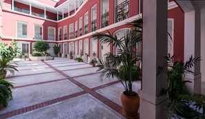 A courtyard with a red and white building, potted plants, and a sign that reads "Corso Santa".