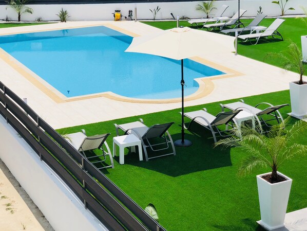 A swimming pool with a surrounding deck, lounge chairs, and a small garden area.