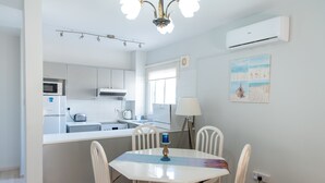 Cocina moderna con armarios blancos, microondas y comedor con mesa y sillas blancas.
