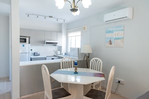 A modern kitchen with white cabinets, a microwave, and a dining area with a white table and chairs.
