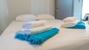 Una cama bien hecha con toallas blancas y azules dobladas, y una toalla azul con flecos.