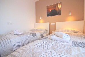 Quarto de hotel com duas camas, cada uma com um edredom estampado e uma toalha enrolada sobre a cama.