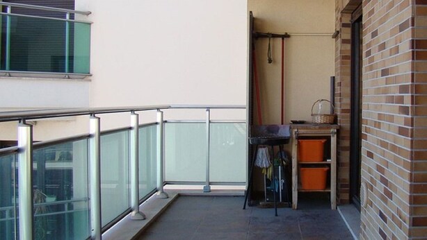 Ein Balkon mit Glastrennwand, einem kleinen Tisch mit Korb und einer Ziegelwand.