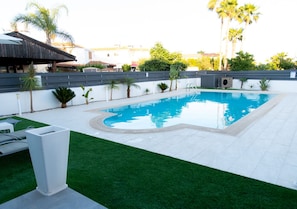 A swimming pool with a curved edge, surrounded by a white wall and a grassy area.