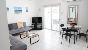 Un salon moderne comprenant un canapé, une table basse, un téléviseur et un coin repas avec des chaises et une table.