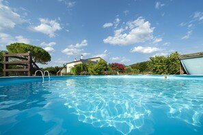 Una piscina cristalina con muelle de madera y una casa al fondo.
