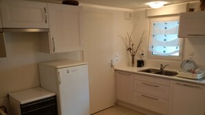 A compact kitchen with white cabinets, a refrigerator, a dishwasher, and a window with a curtain.