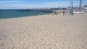 A sandy beach with people, boats, and a pier in the background.