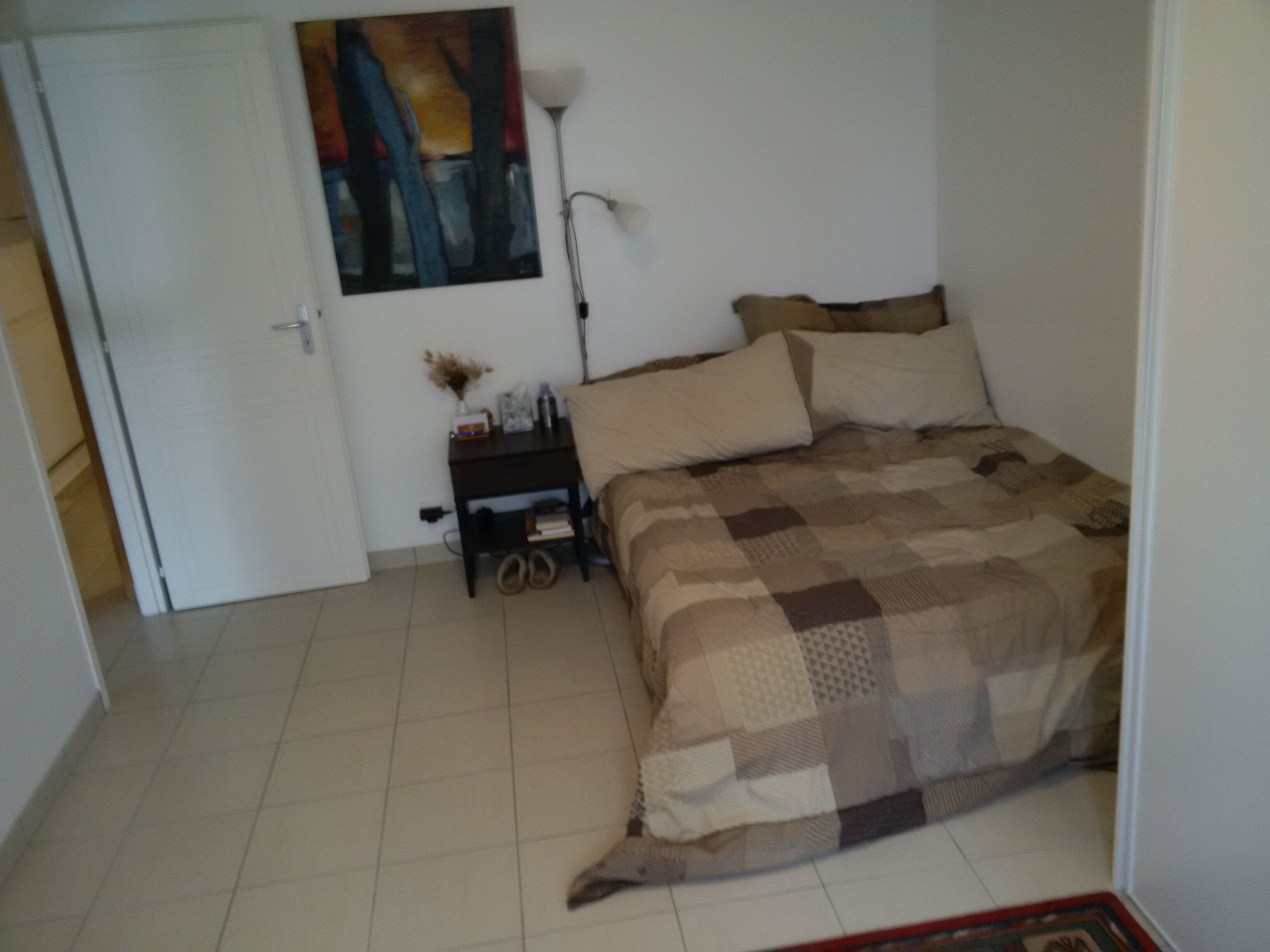 Una camera da letto con un letto, un comodino, una lampada e un quadro appeso al muro.