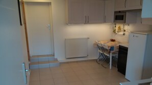 A kitchen with white cabinets, a tiled floor, a dining table with chairs, a microwave, and a refrigerator.