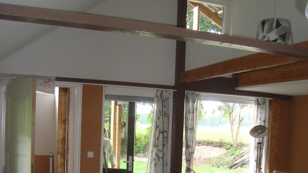 A spacious living area with a high ceiling, wooden beams, a black leather sofa, a yellow armchair, and a view of a garden through large glass doors. - Holiday home / B & B 't Zwaluwnest - peace, space and privacy with its own sauna (Luttenberg)