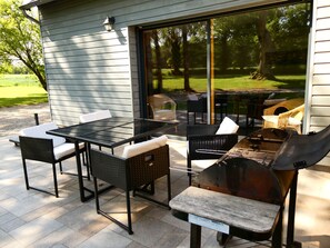 Una veranda esterna con barbecue, mobili in vimini e una porta vetrata che dà su un giardino.