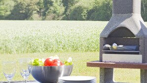 An outdoor dining setup with a stone grill, a bowl of salad, plates, and glasses on a table.