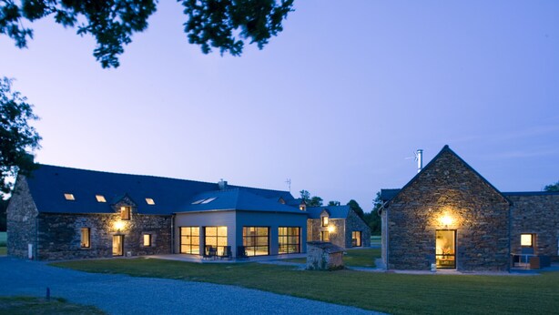 A stone building with multiple windows and a sloped roof, surrounded by a well-maintained lawn.
