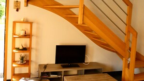 A modern living room with a wooden staircase, a flat-screen TV, a wooden coffee table, and a bookshelf.