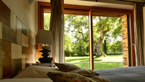 A bedroom with a bed, a lamp, and a view of a garden through a window.