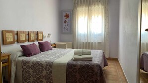 Un dormitorio con una cama, dos mesitas de noche, una lámpara, una ventana con cortinas y decoración en la pared.