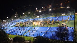 Un court de tennis comprenant plusieurs terrains, entouré d’une clôture et éclairé par des projecteurs.