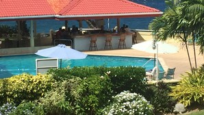 A poolside bar with a red roof, overlooking a pool and the ocean.